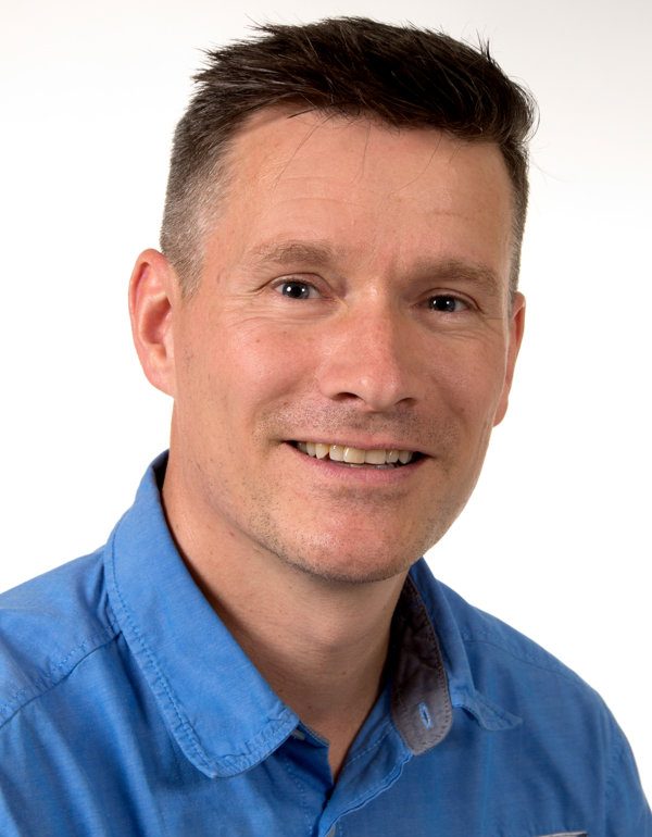 Porträt eines lächelnden Mannes mit kurzen, hellen Haaren und blauer Hemd.